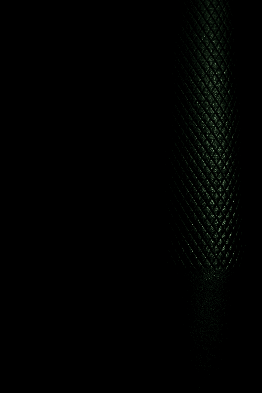 Close-up dumbbell macro with subtle green rim light on dark background.